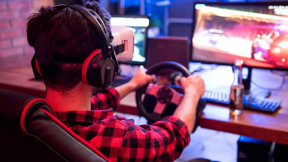 Een persoon met een VR-bril en koptelefoon zit in een gamestoel en gebruikt een stuur voor een computerspel.