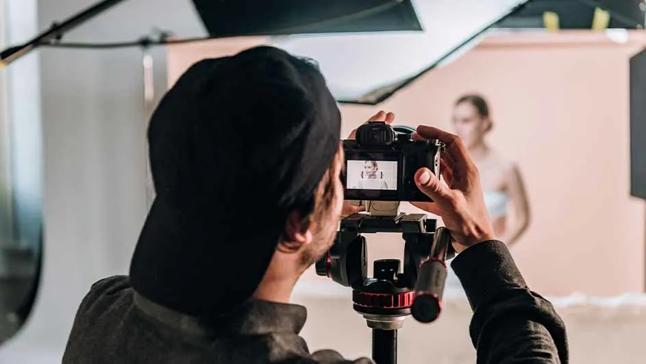 Een fotograaf met een pet gebruikt een camera op een statief in een studio met een vrouw als model.