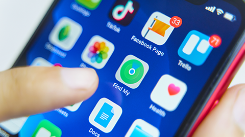 Een vinger tikt op een blauw smartphonescherm met app-pictogrammen, waaronder TikTok, Facebook, Trello en Find My.