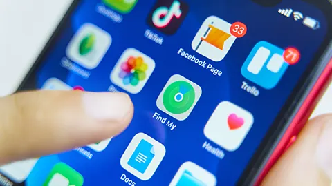 Een vinger tikt op een blauw smartphonescherm met app-pictogrammen, waaronder TikTok, Facebook, Trello en Find My.