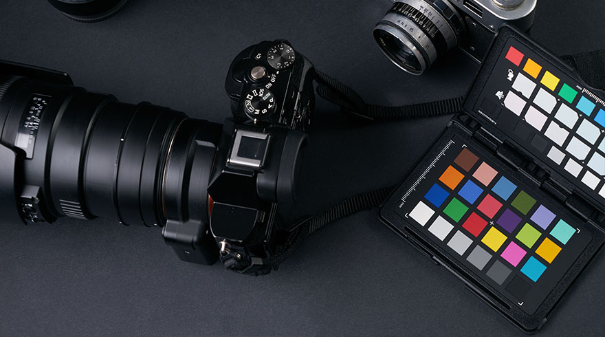 Een zwarte camera met een grote lens, een vintage camera en een kleurkalibratiekaart liggen op een zwarte achtergrond.