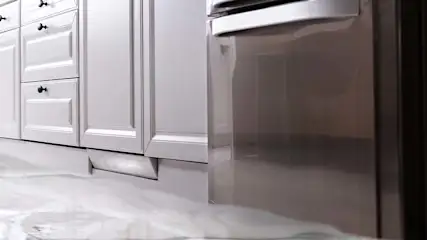 Witte keukenkasten met zwarte knoppen en een roestvrijstalen vaatwasser staan op een witte vloer met gemarmerd patroon.