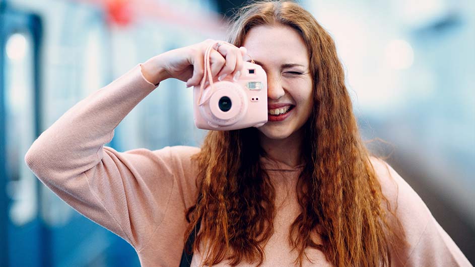 Een lachende vrouw houdt een roze camera voor haar gezicht in een omgeving met blauwe tinten.