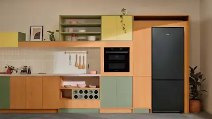 Een keuken met houten kasten, een zwarte koelkast, een oven en groene accenten.
