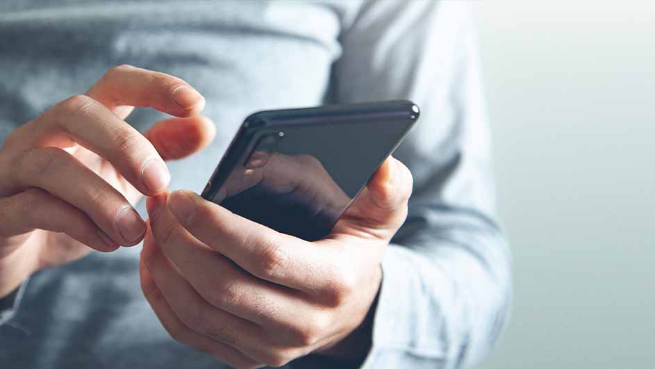 Een persoon in een grijs overhemd houdt een zwarte smartphone vast en gebruikt deze.