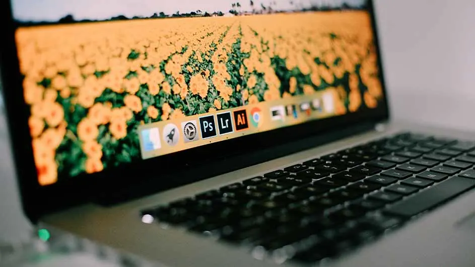 Een laptop met een zwart toetsenbord toont een veld met gele bloemen op het scherm en app-pictogrammen onderaan.