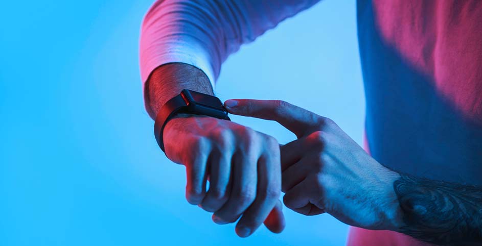 Een persoon met een smartwatch tikt erop met een vinger, tegen een blauwe en roze achtergrond.