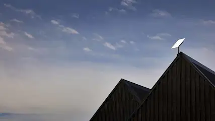 Houten gebouwen met puntige daken tegen een lucht met blauwe en witte wolken, met een witte antenne op een van de daken.