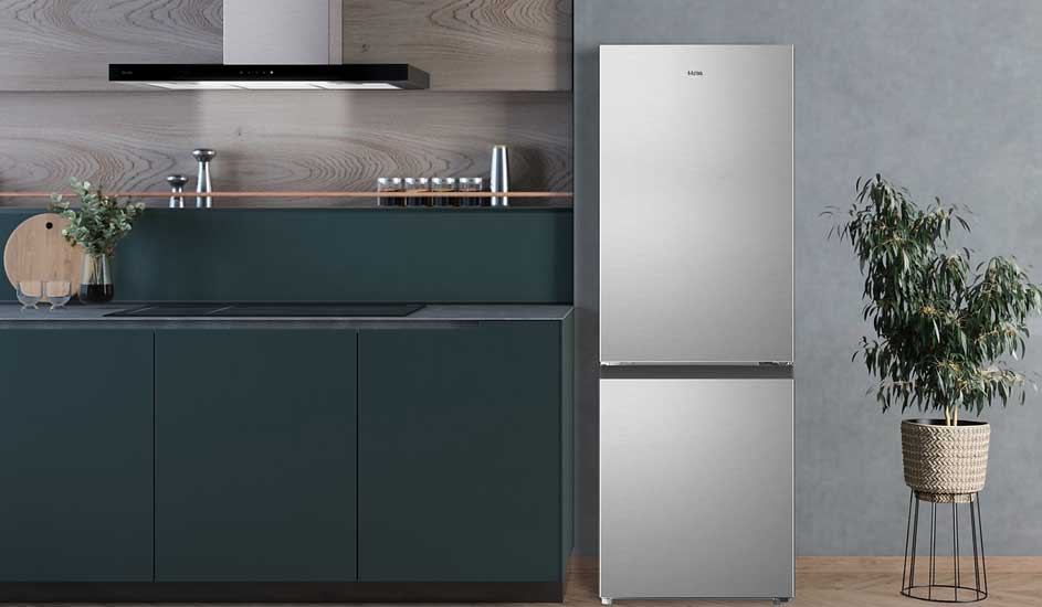 Een moderne keuken met een zilveren Hisense koelkast met ondervriesvak, groene kasten en een plant in een mand op standaard naast de koelkast.