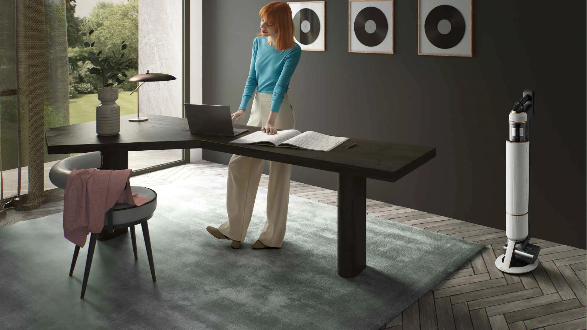 Een vrouw staat aan een bureau met een laptop en een open boek, met een stofzuiger op de achtergrond.