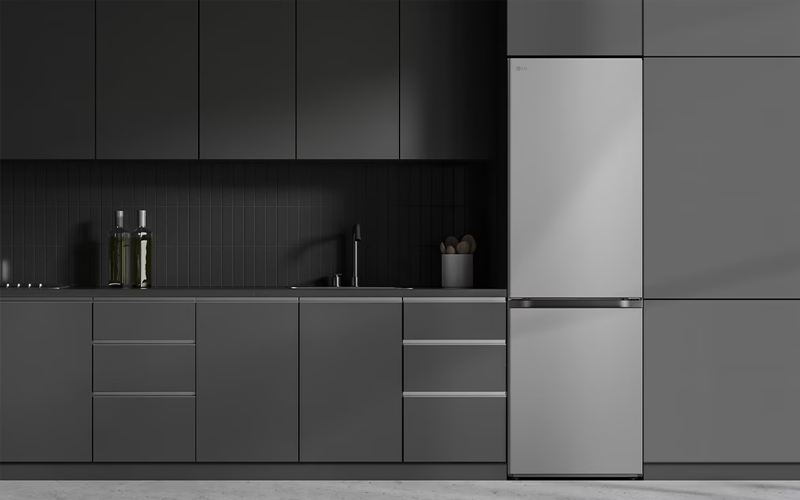 Moderne keuken met matgrijze keukenkasten, een zilverkleurige koelkast, een zwarte gootsteen en enkele flessen en een pot op het aanrecht.