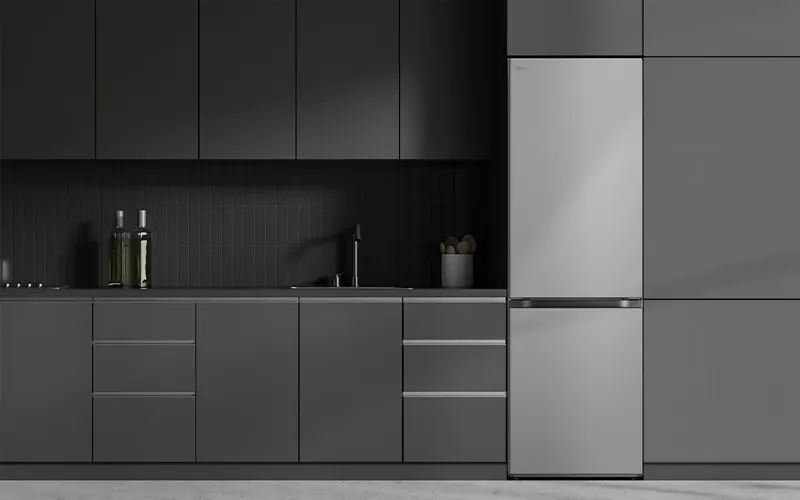 Moderne keuken met matgrijze keukenkasten, een zilverkleurige koelkast, een zwarte gootsteen en enkele flessen en een pot op het aanrecht.