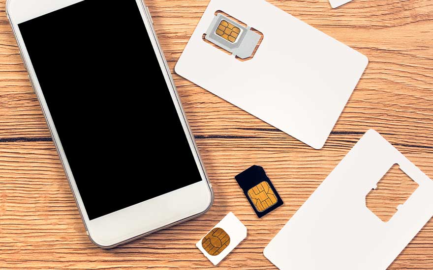 Witte smartphone op houten tafel met verschillende SIM-kaarten en adapters uitgespreid voor installatie en gebruik.