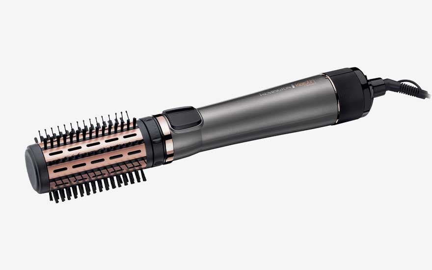 Grey hot air brush with rose gold barrel and short plastic bristles lies horizontally, combining blow drying power and volumising brush in one tool.