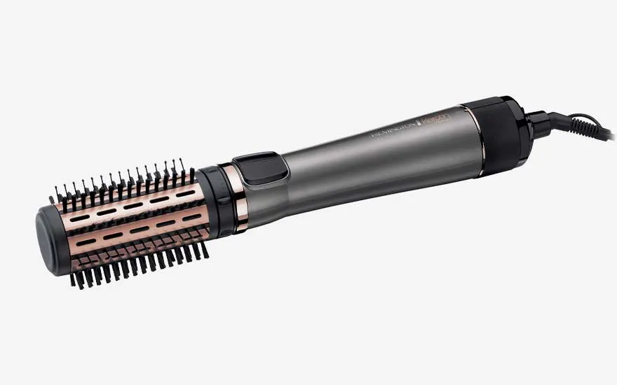 Grey hot air brush with rose gold barrel and short plastic bristles lies horizontally, combining blow drying power and volumising brush in one tool.