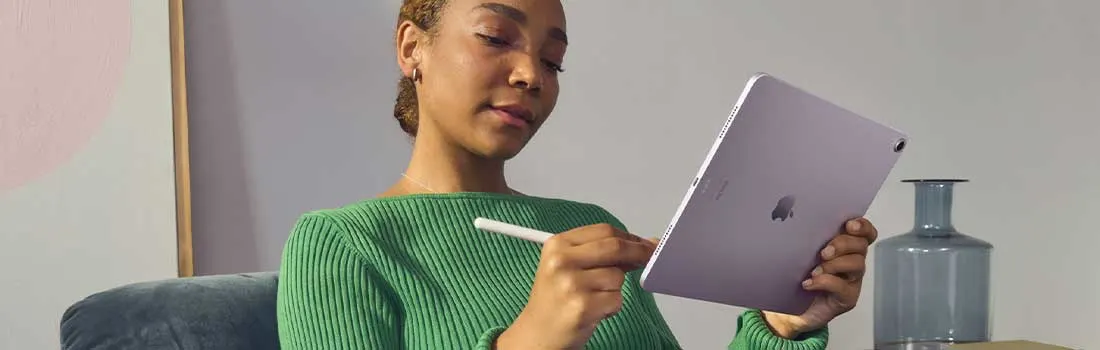 Vrouw ontspant op een bank en gebruikt een paarse tablet met stylus, geconcentreerd schrijvend of tekenend in een rustige woonkamer.