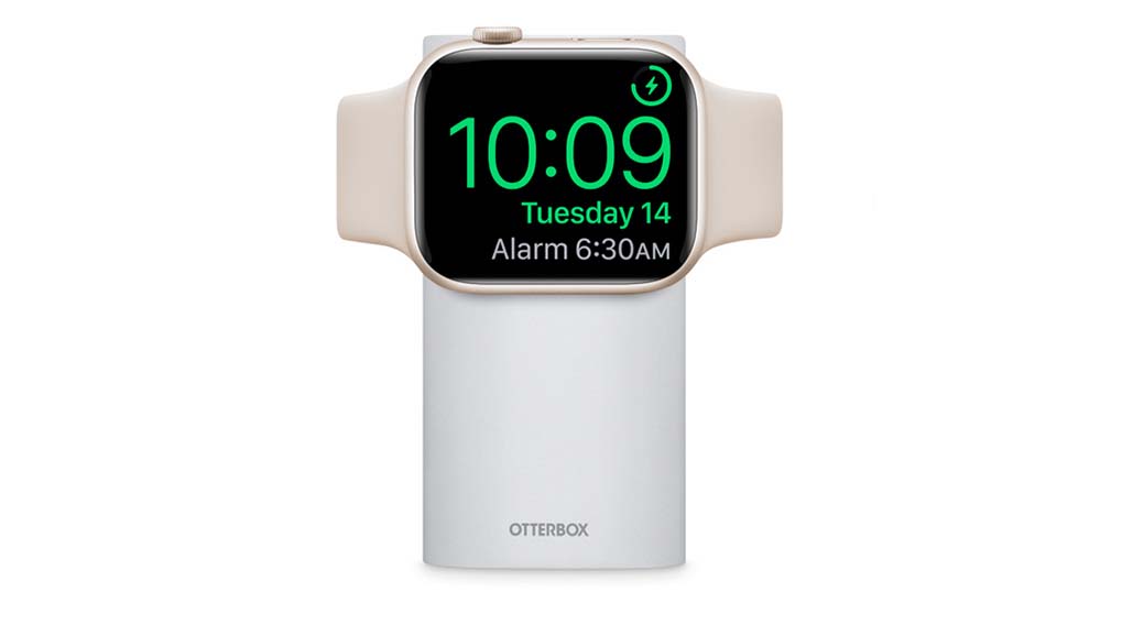 Een smartwatch met een lichtgekleurde band ligt op een witte Otterbox oplader, met een groene tijdsaanduiding van 10:09.