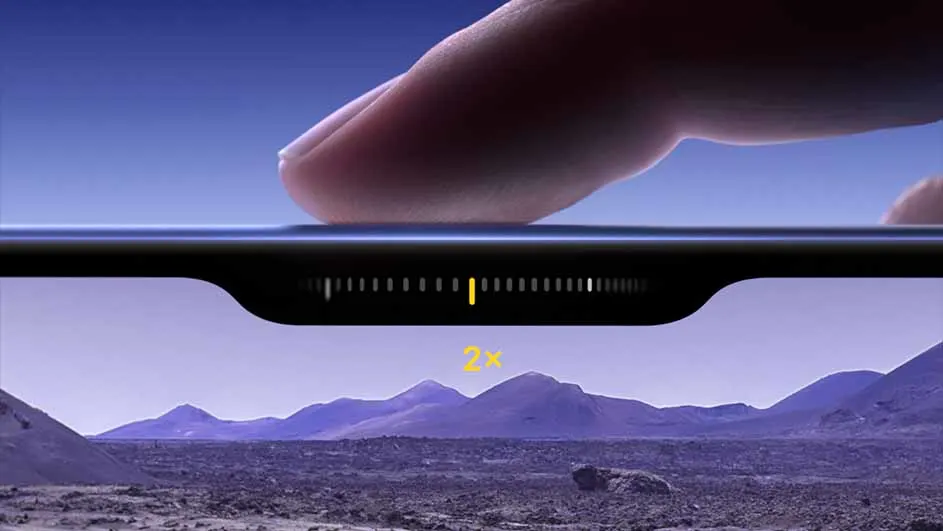 Vinger op zwarte telefoon, zoomindicator zichtbaar. Achtergrond: paarskleurig berglandschap onder blauwe lucht.