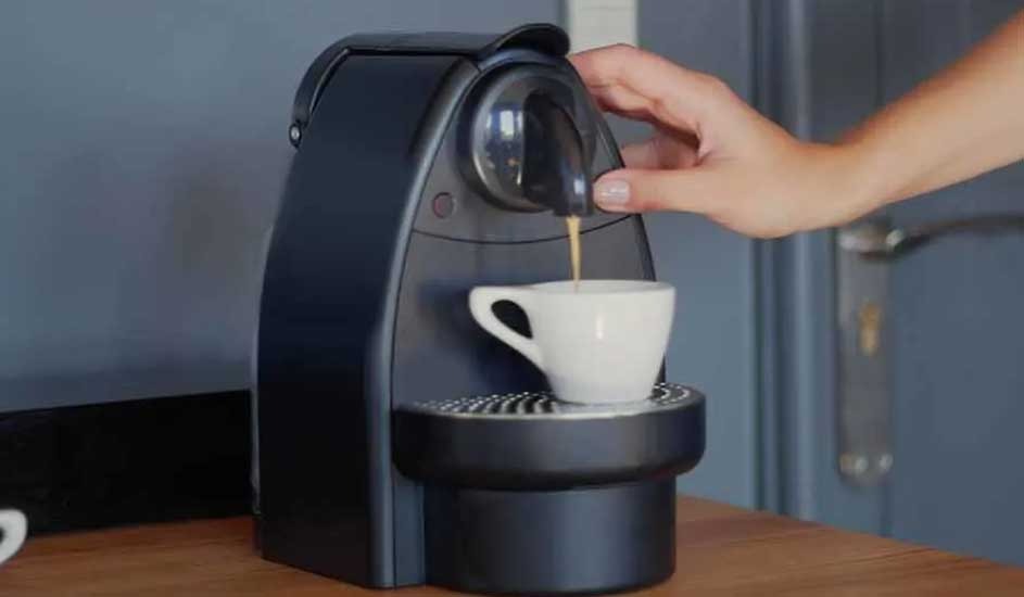 A Nespresso coffee machine pours fresh espresso into a white cup, placed on a wooden counter in a modern kitchen setting.