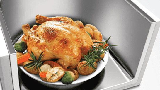 Een gebraden kip en groenten op een wit bord in een roestvrijstalen gootsteen.