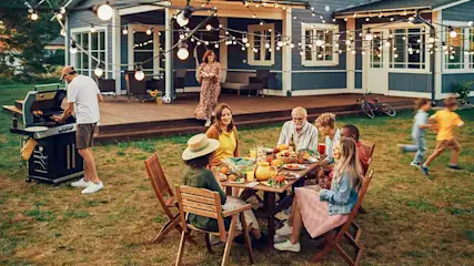 Een familie geniet van een barbecue in de tuin, terwijl kinderen spelen en lichtslingers een warme, feestelijke sfeer geven.