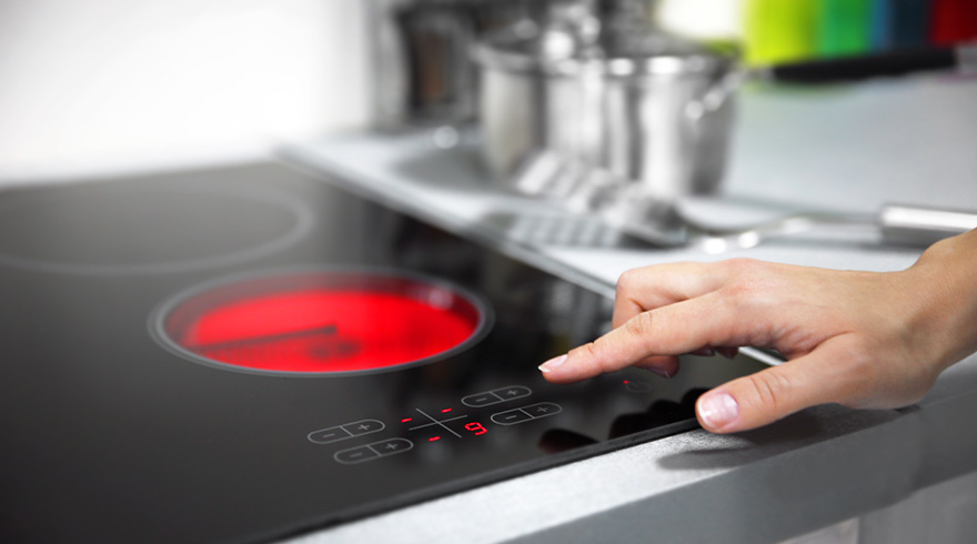 Een hand bedient een zwarte inductiekookplaat met een rode gloeiende kookzone en digitale display.