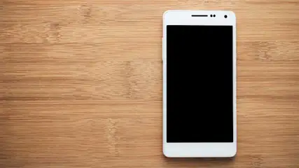 Een witte smartphone met een zwart scherm ligt op een houten oppervlak.