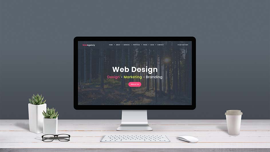 Een computerscherm toont webdesign, op een wit bureau met een toetsenbord, muis, planten, bril en een beker.