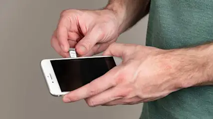 Een hand plaatst een simkaart in een witte smartphone. De achtergrond is effen grijs.
