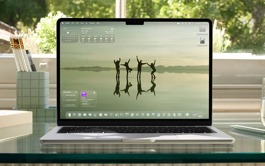 MacBook toont desktop met silhouetten van springende mensen bij water, kalender widget, groene accessoires op bureau.