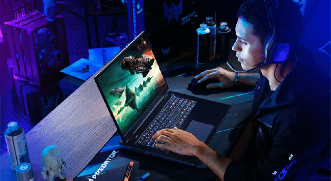 Een man met een koptelefoon gebruikt een laptop met een videogame erop, op een bureau met flessen en decoraties.