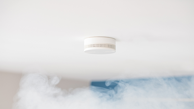 Rookmelder aan wit plafond. Op de achtergrond is er rook.