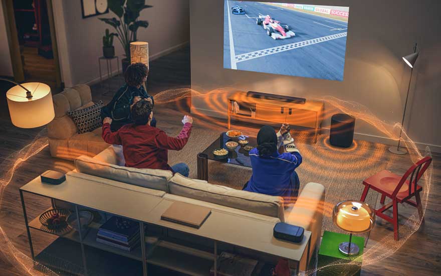 Gezin kijkt racewedstrijd via projector, met soundbar en subwoofer; oranje golven verbeelden surroundgeluid in de kamer.