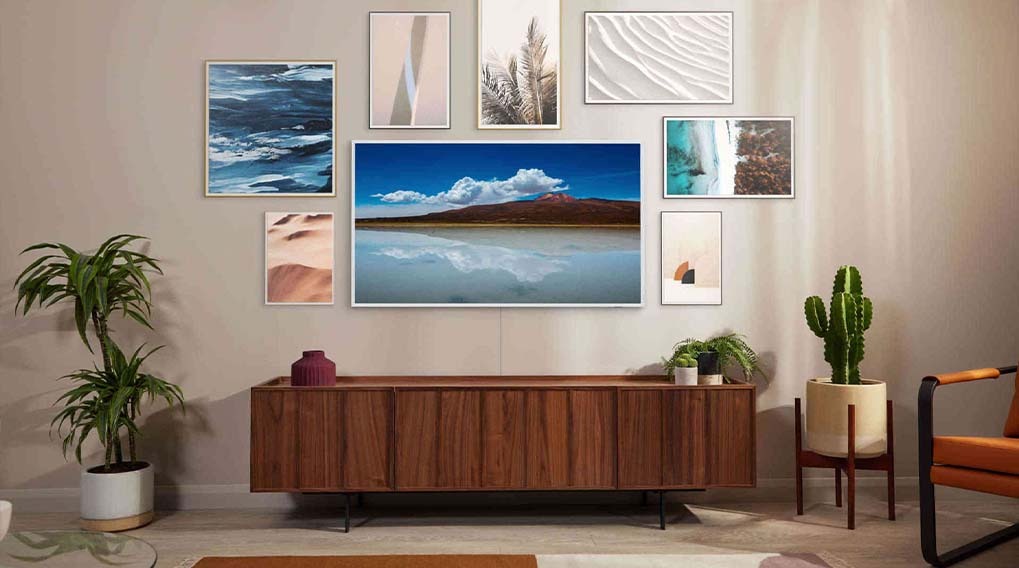Living room with a TV above a wooden cabinet, surrounded by framed art, plants, and a chair.