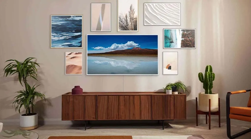 Living room with a TV above a wooden cabinet, surrounded by framed art, plants, and a chair.