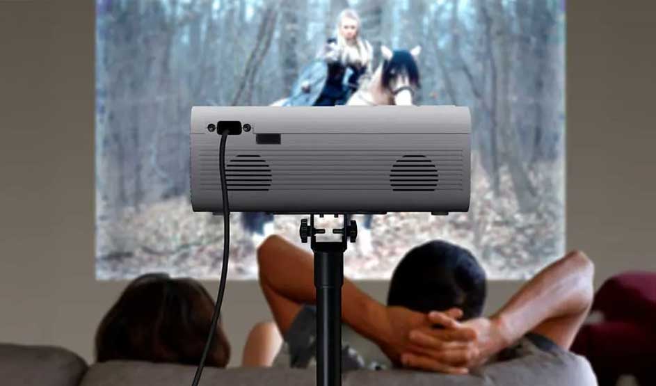Een projector op een statief toont een film, terwijl twee mensen ontspannen kijken vanuit een woonkamer.