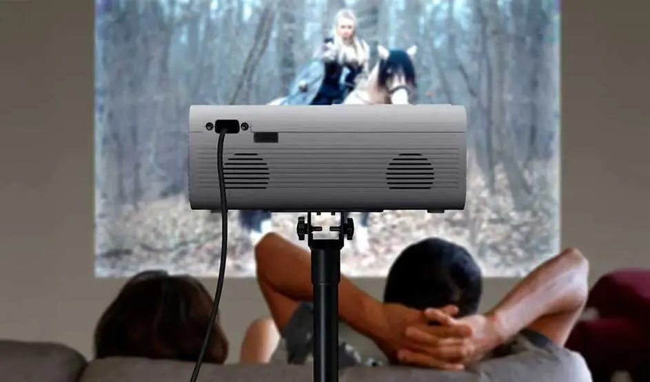 Een projector op een statief toont een film, terwijl twee mensen ontspannen kijken vanuit een woonkamer.