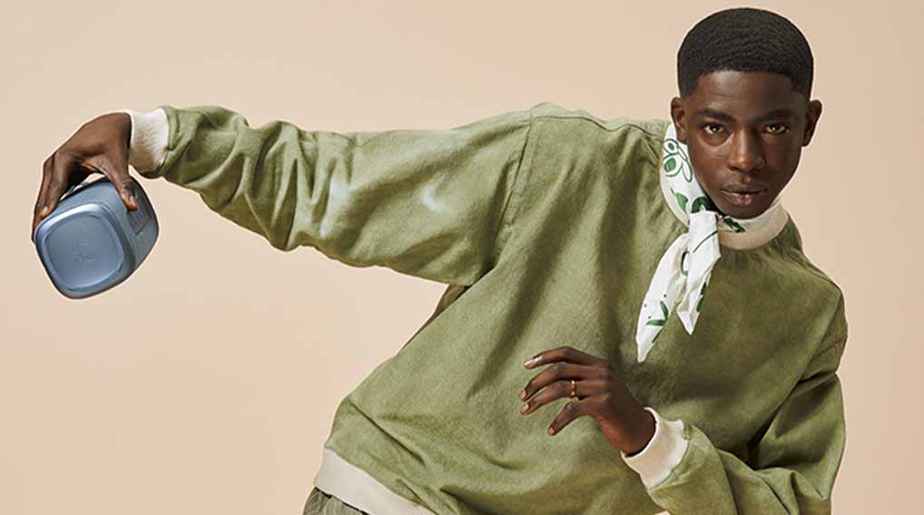 Een persoon in een olijfgroen shirt houdt een grijze kubus vast en draagt ​​een witte sjaal met groene patronen.