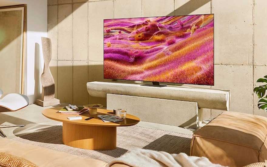 Moderne woonkamer met grote TV die levendig paars-oranje landschap toont, beige bank, houten salontafel en warme zonlichtinval.