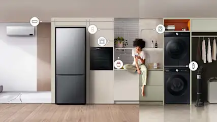 Een keuken met een koelkast, oven en een vrouw die op een aanrecht zit met een telefoon. Er staat een wasmachine en droger.
