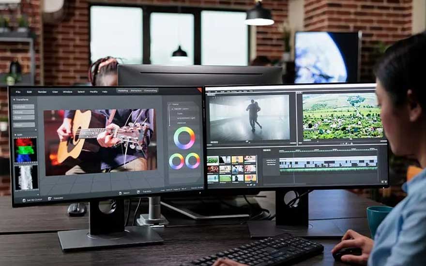 In a brick studio an editor works on dual widescreen monitors, fine tuning colour wheels and arranging video clips on timelines.