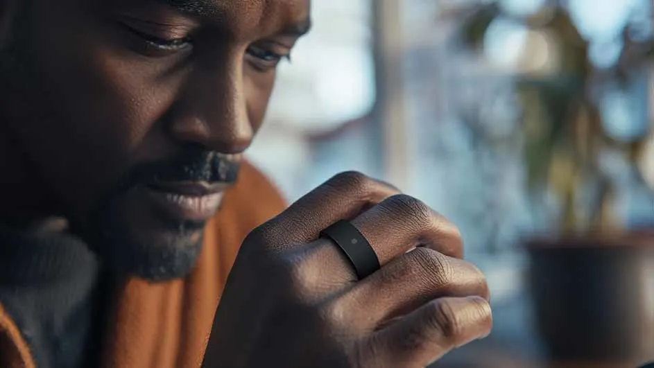 Een man kijkt naar een zwarte ring met een sensor aan zijn vinger, met een plant op de achtergrond.
