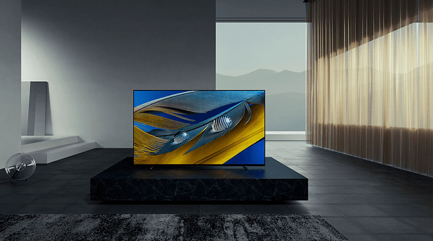Een tv staat op een zwarte sokkel in een kamer met een groot raam en gordijnen. Op het scherm een abstract blauw en geel patroon.