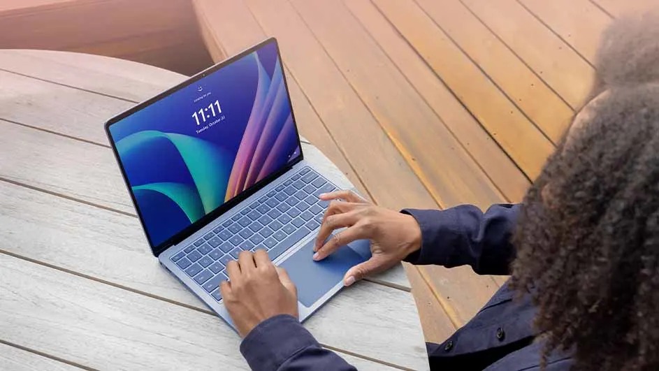 Een persoon typt op een open ASUS laptop aan een ronde tafel buiten op een terras. Het scherm toont de tijd. Merknaam: ASUS.