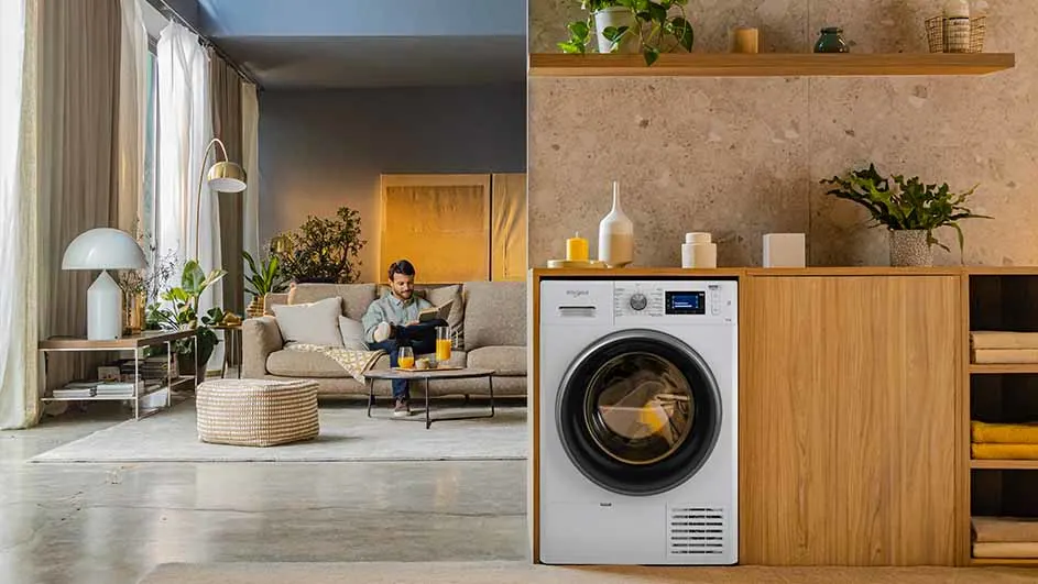 Woonkamer met man op bank en wasmachine in houten kast, planten en decoraties op plank.