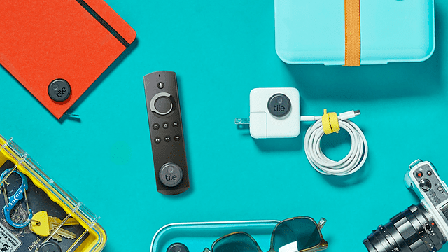 Oranje notitieboek, afstandsbediening, witte oplader, camera en zonnebril op een blauwe achtergrond.