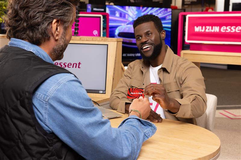 Twee mensen zitten aan een ronde tafel. De een geeft een rode kaart aan de ander voor een computer met het woord 'essent'.