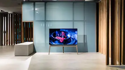 Een tv staat in een kamer met houten lamellen en een blauwe muur. Het scherm toont fruit.