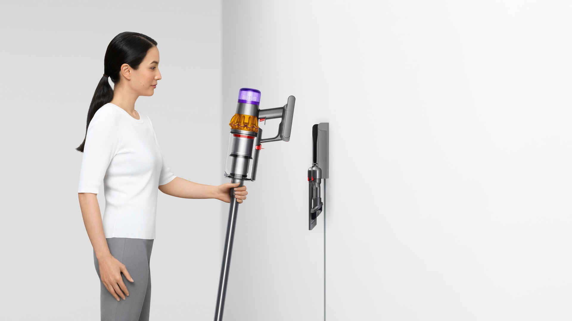 Een vrouw houdt een stofzuiger vast bij een witte muur met een oplaadstation.