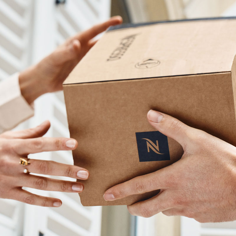 Een kartonnen doos met een Nespresso logo wordt door twee handen vastgehouden.